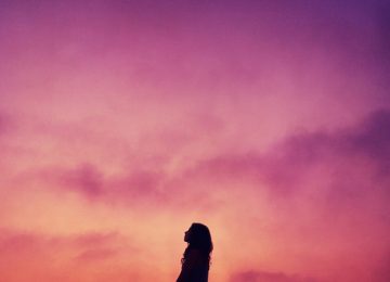 Silhouet van vrouw tegen een paarsgekleurde hemel, de vrouw lijkt eenzaam